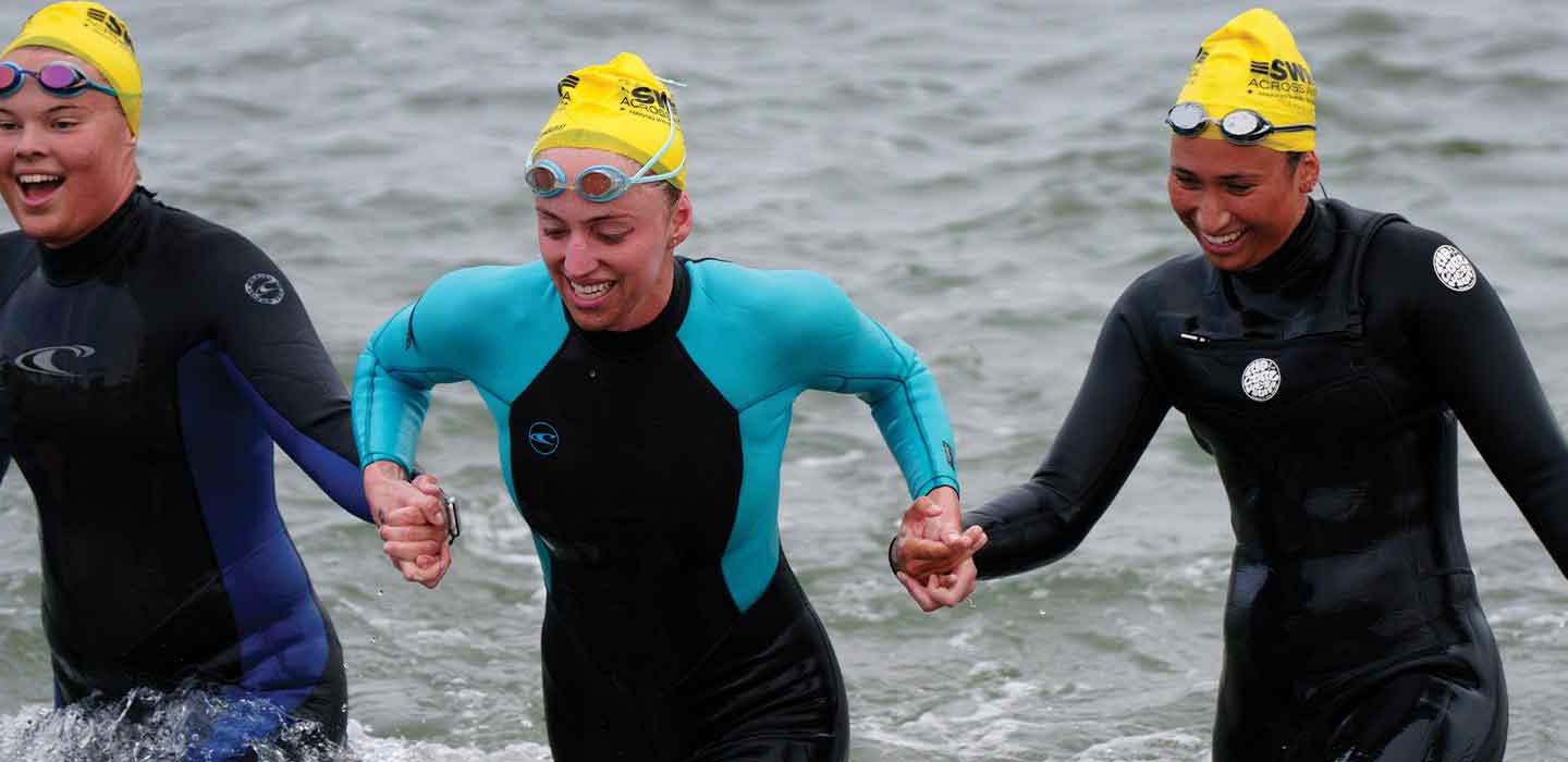 a trio of swimmers hold hands coming out of the water