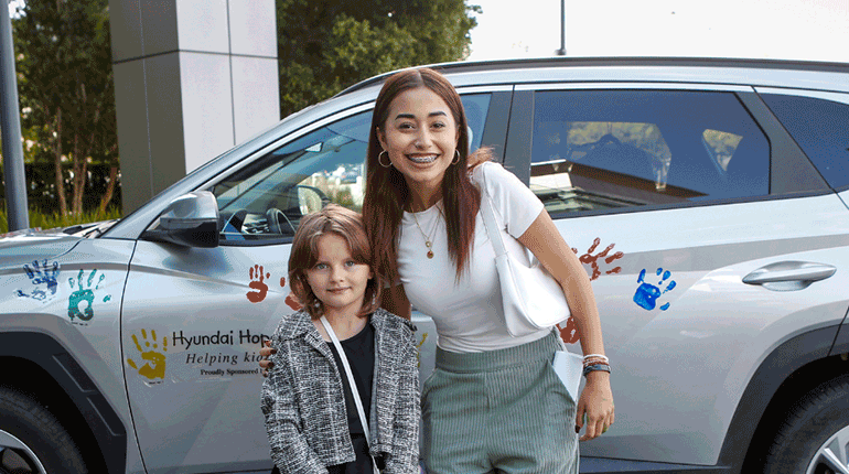 two patient ambassadors stand in front of a car