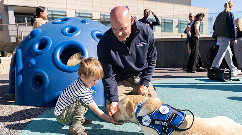 a patient smiles with a facility dog on the playground