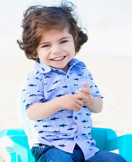 Julian faces the camera smiling in a blue chair on the beach 