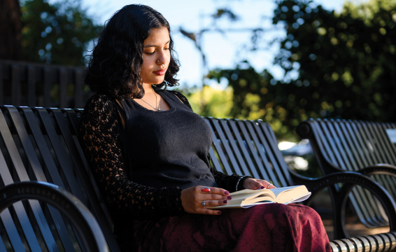 a teen sits on a park bench reading a book