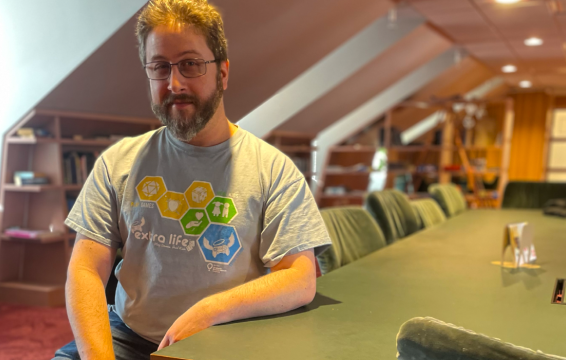 Jesse sits at a desk wit han extra life tee on