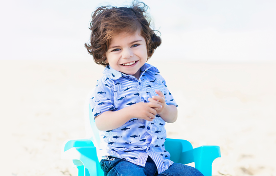 Julian faces the camera smiling in a blue chair on the beach