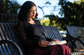 a teen sits on a park bench reading a book