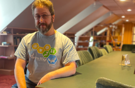 Jesse sits at a desk wit han extra life tee on