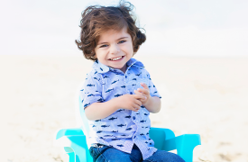 Julian faces the camera smiling in a blue chair on the beach 